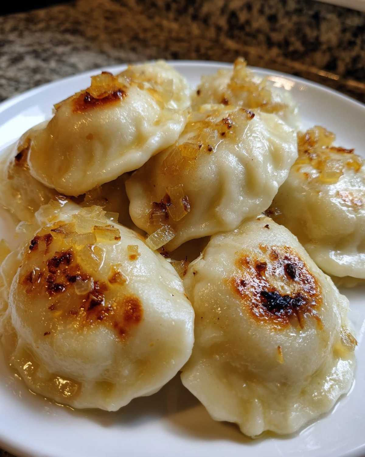 Zbliżenie na talerz pełen gotowych Pierogi ruskie domowe polane skarmelizowaną cebulką.