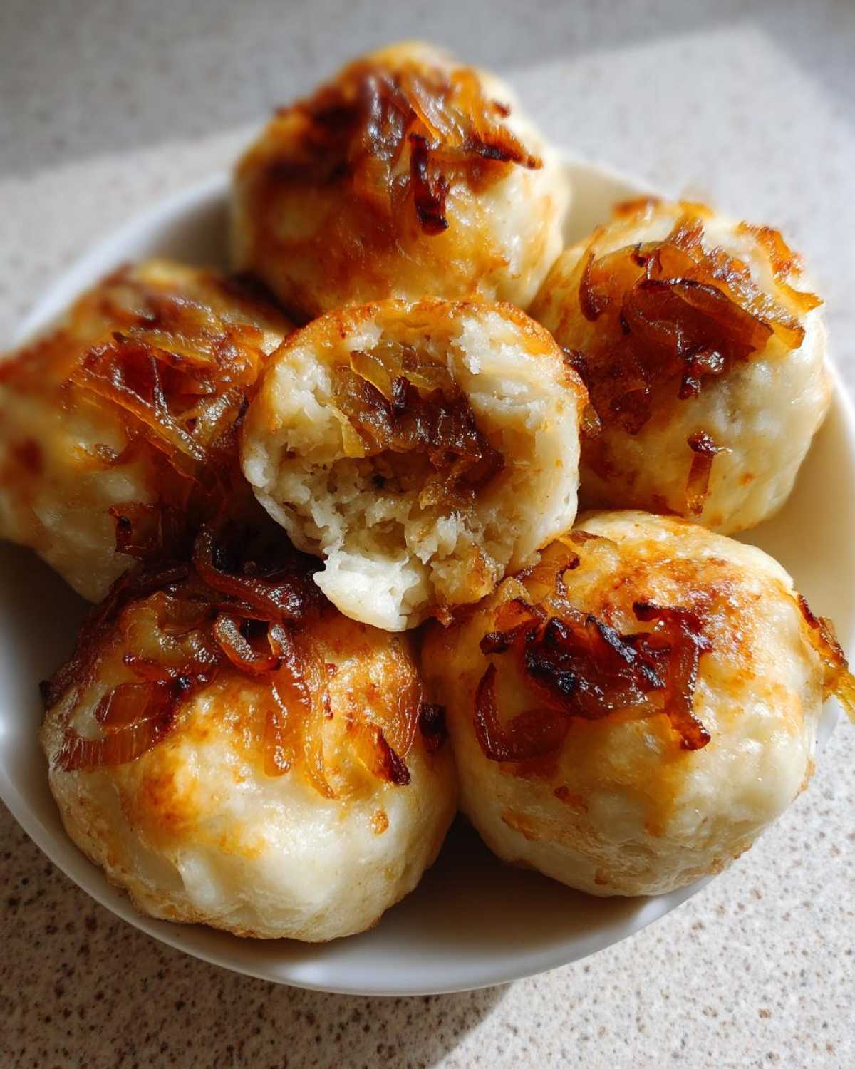 Zbliżenie na talerz z pierogami z mięsem z rosołu, polanymi skarmelizowaną cebulką.