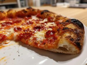 Zbliżenie na kawałek Pepperoni Pizza w kształcie serca z puszystym, przypieczonym brzegiem i ciągnącym się serem.