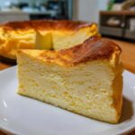 Kawałek puszystego Sernika wiedeńskiego bez spodu z przypieczoną górą na białym talerzu.