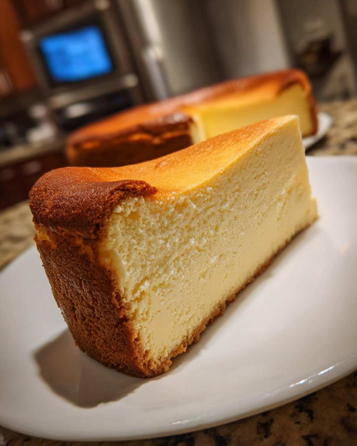 Zbliżenie na kawałek kremowego Sernika wiedeńskiego bez spodu z pięknie zrumienioną skórką.