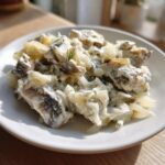 Porcja śledzie w śmietanie z jabłkiem i cebulą, udekorowana koperkiem, na białym talerzu.