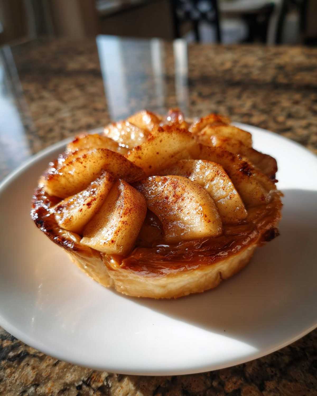 Pojedyncze, karmelizowane szybkie ciastka francuskie z jabłkami posypane cynamonem na białym talerzu.