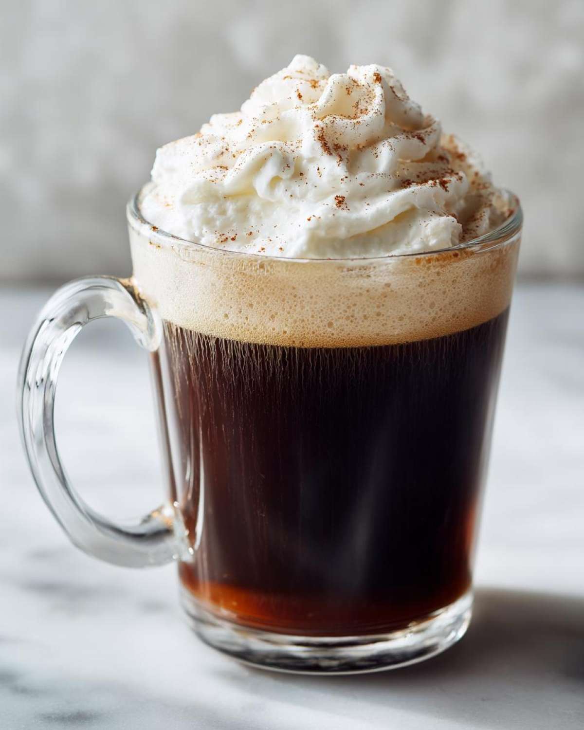 Szklany kubek Zimowa kawa z przyprawami zwieńczona bitą śmietaną i cynamonem.
