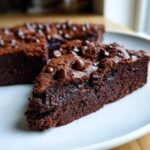 Zbliżenie na wilgotny kawałek Brownie z fasoli czerwonej posypany kroplami czekolady na białym talerzu.