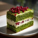 Kawałek Ciasta Leśny Mech z zielonym biszkoptem, białą masą i pestkami granatu na wierzchu.