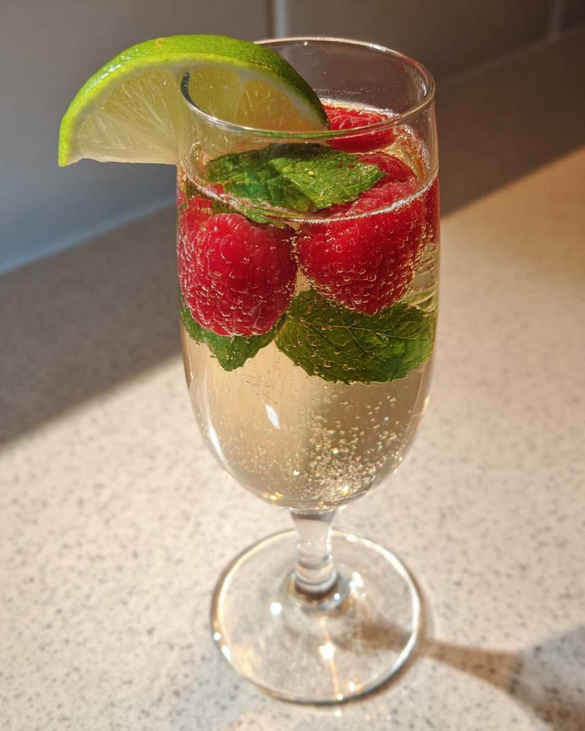Kieliszek musującego drinka z Prosecco z malinami, miętą i plasterkiem limonki.