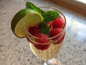 Zbliżenie na kieliszek musującego drinka z Prosecco, udekorowanego malinami, listkami mięty i plasterkiem limonki.