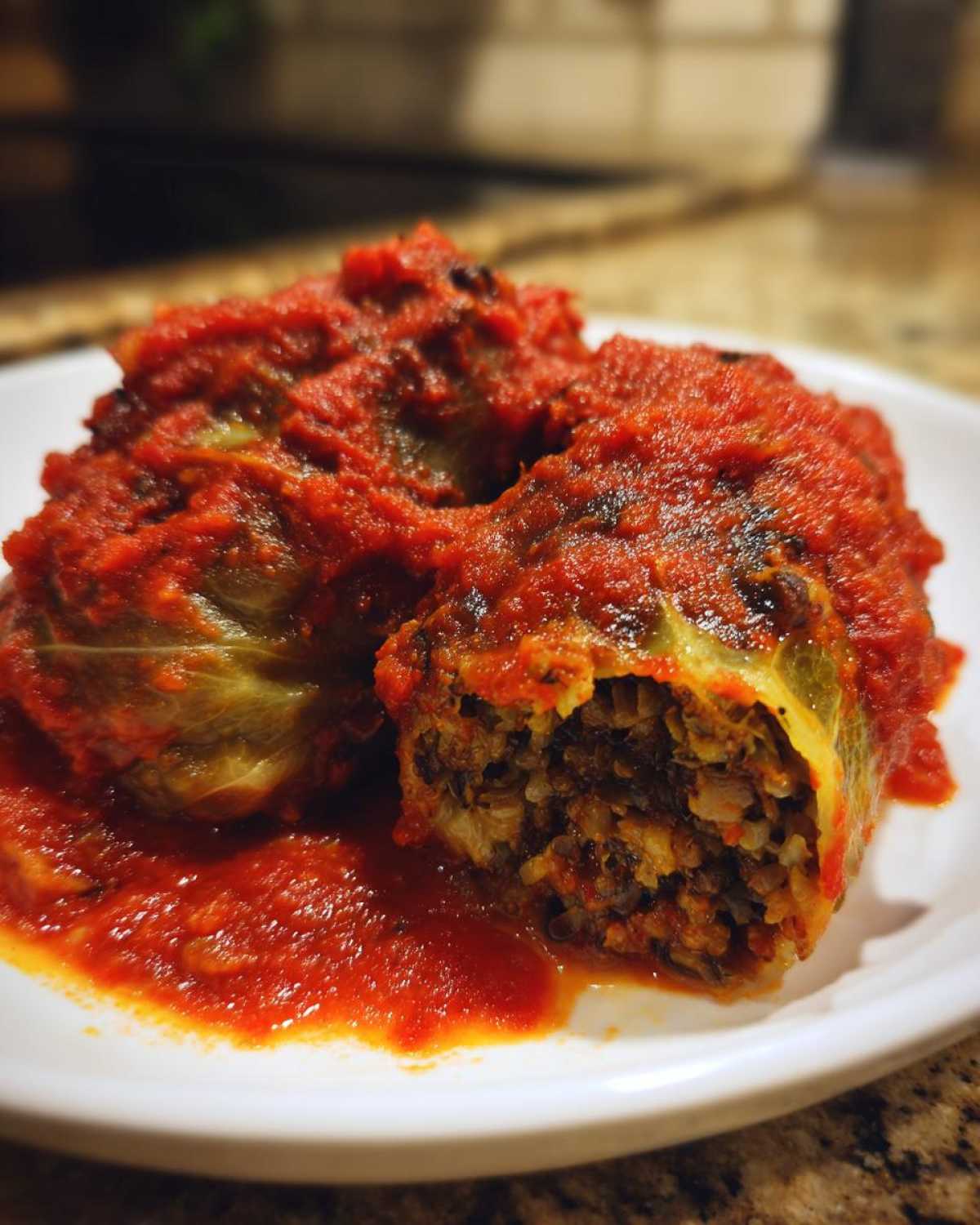 Zbliżenie na Gołąbki z kaszą i pieczarkami polane obficie czerwonym sosem pomidorowym na białym talerzu.