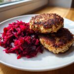 Dwa złociste kotlety mielone ułożone obok porcji intensywnie czerwonych buraczków na białym talerzu.