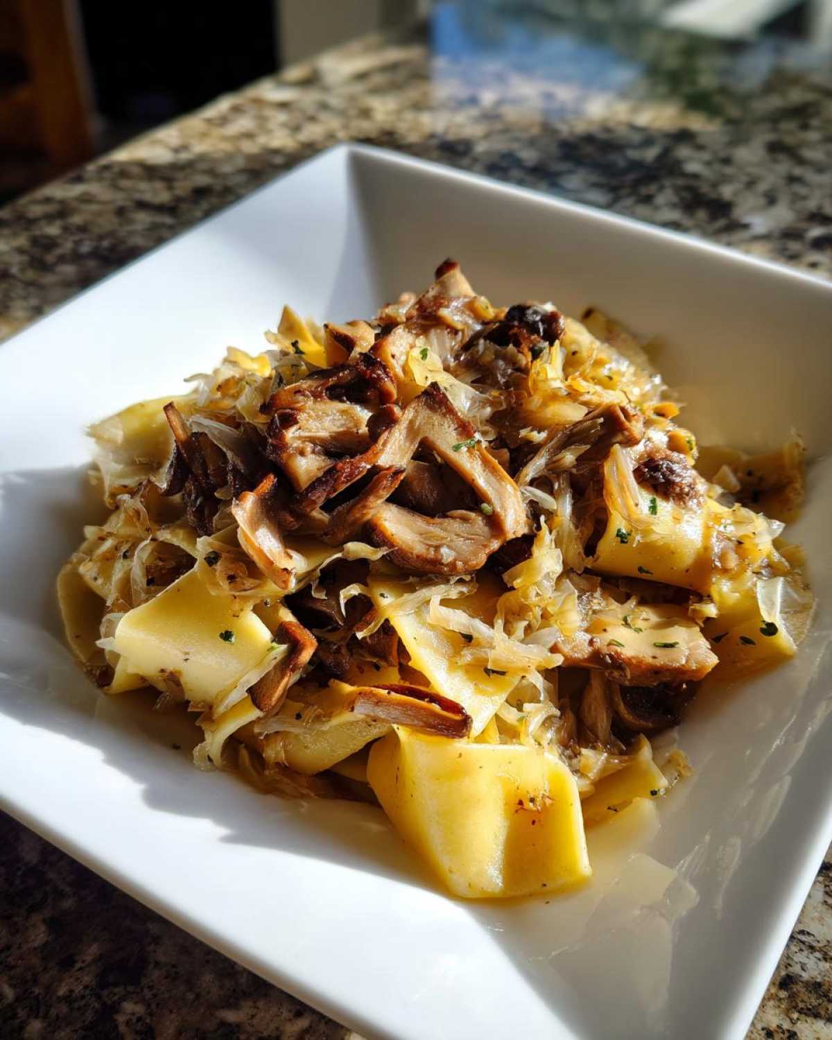 Porcja domowych łazanki z kapustą i pieczarkami podana w kwadratowej, białej misce.