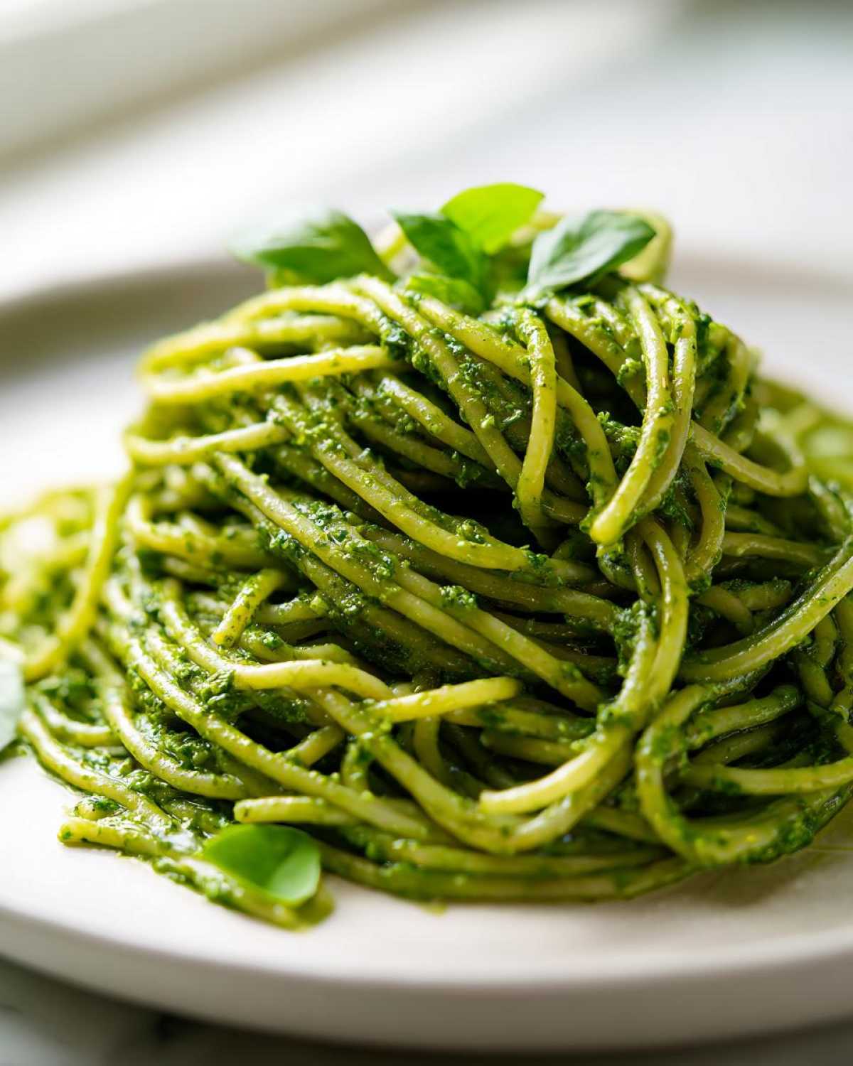 Zbliżenie na porcję spaghetti obficie polaną intensywnie zielonym makaronem z pesto (zielonym).