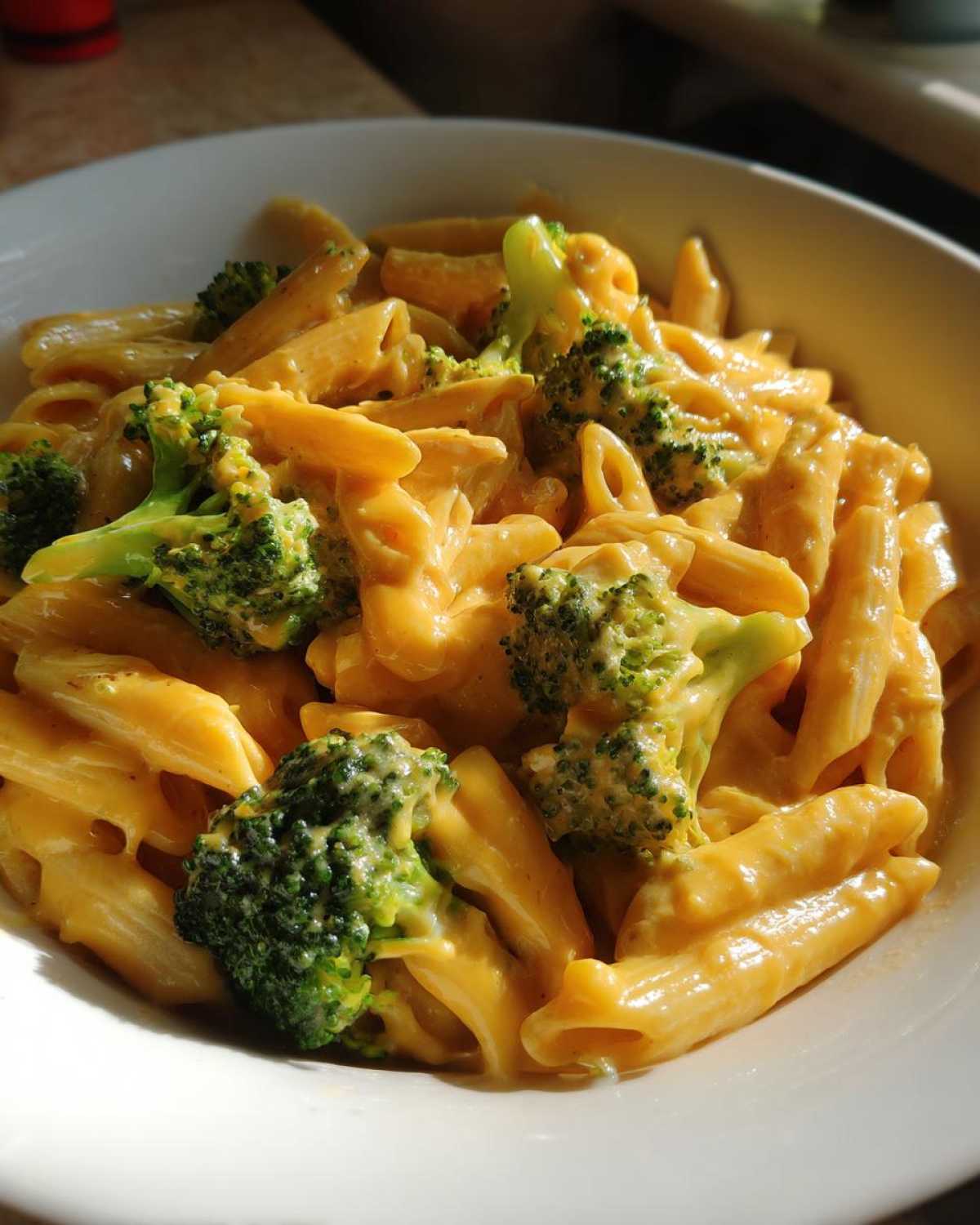 Zbliżenie na penne makaron z sosem serowym i kawałkami brokułów w białej misce.