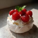 Zbliżenie na jedną mini pavlovę z owocami, bitą śmietaną i listkiem mięty.