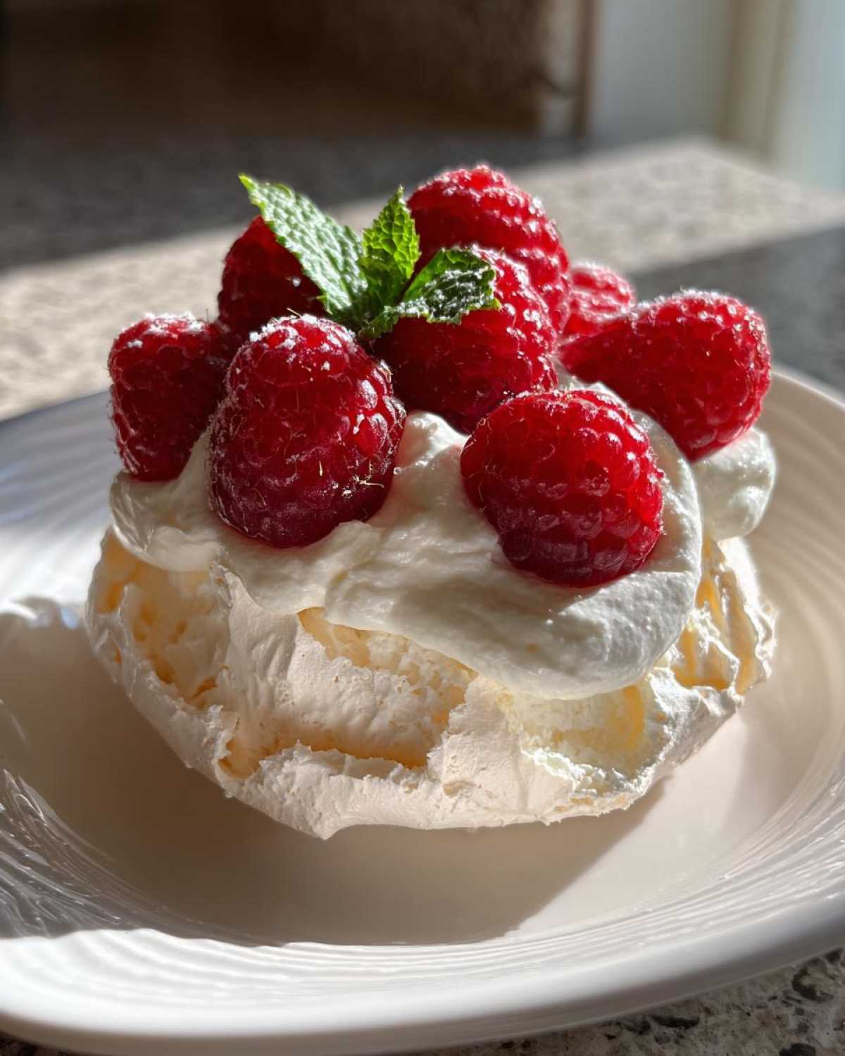 Zbliżenie na jedną Mini pavlova z owocami: beza, bita śmietana, maliny i listek mięty.