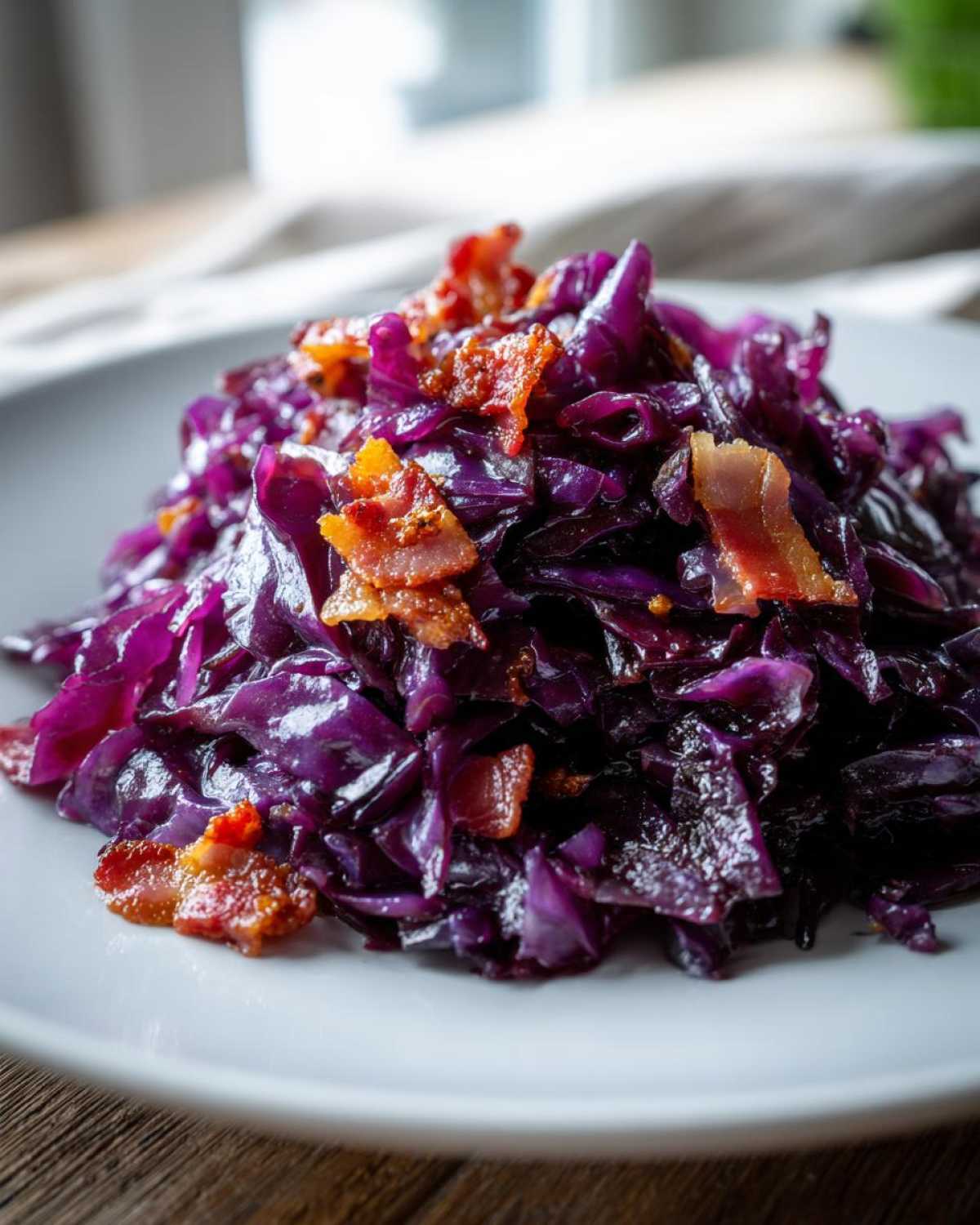 Zbliżenie na talerz z purpurową, duszona modra kapusta zasmażana, posypana chrupiącym boczkiem.