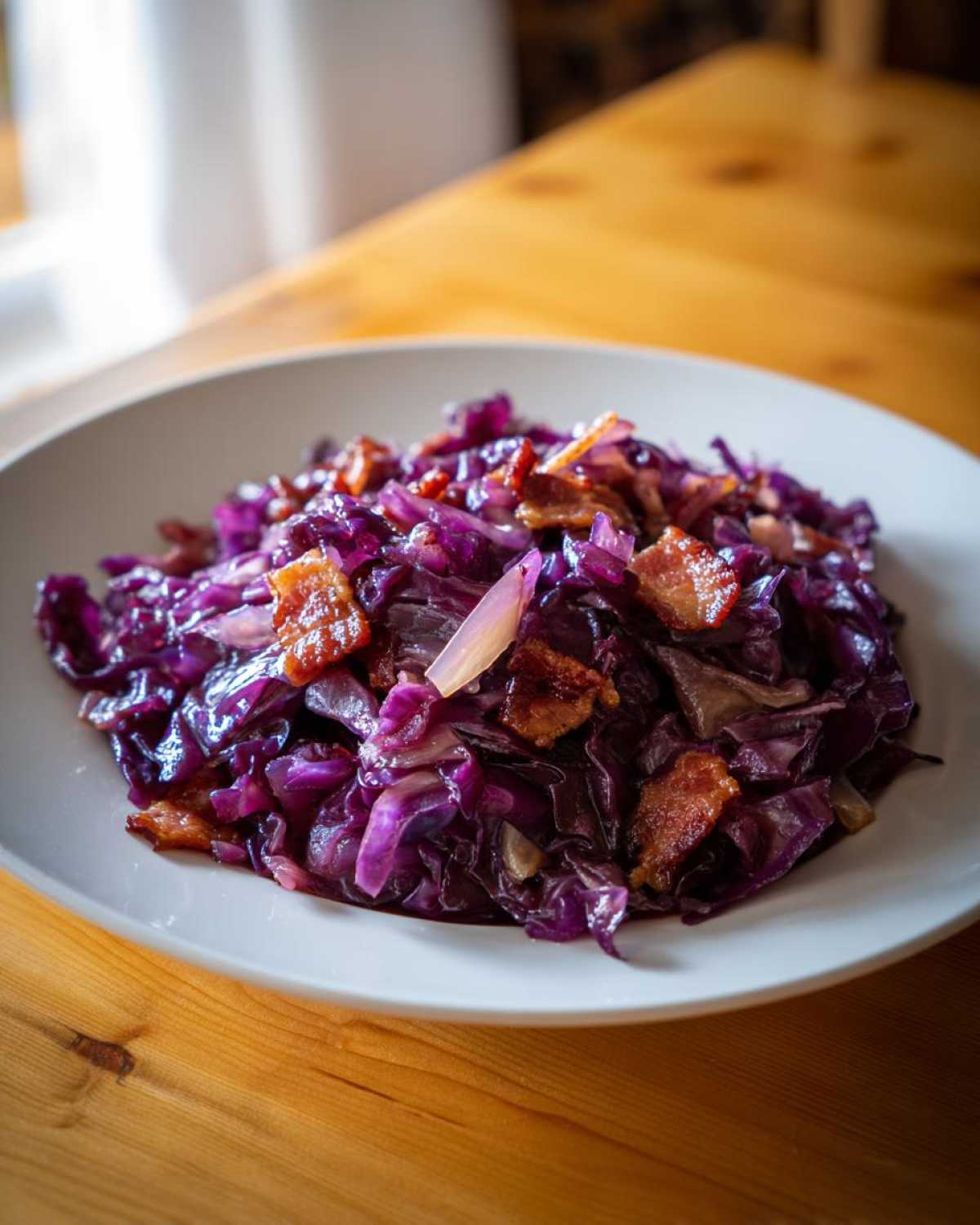 Porcja Modra kapusta zasmażana podana na białym talerzu, z kawałkami chrupiącego boczku.