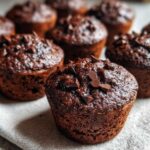 Zbliżenie na wilgotne Muffinki czekoladowe z kawałkami czekolady, ułożone na jasnej ściereczce.
