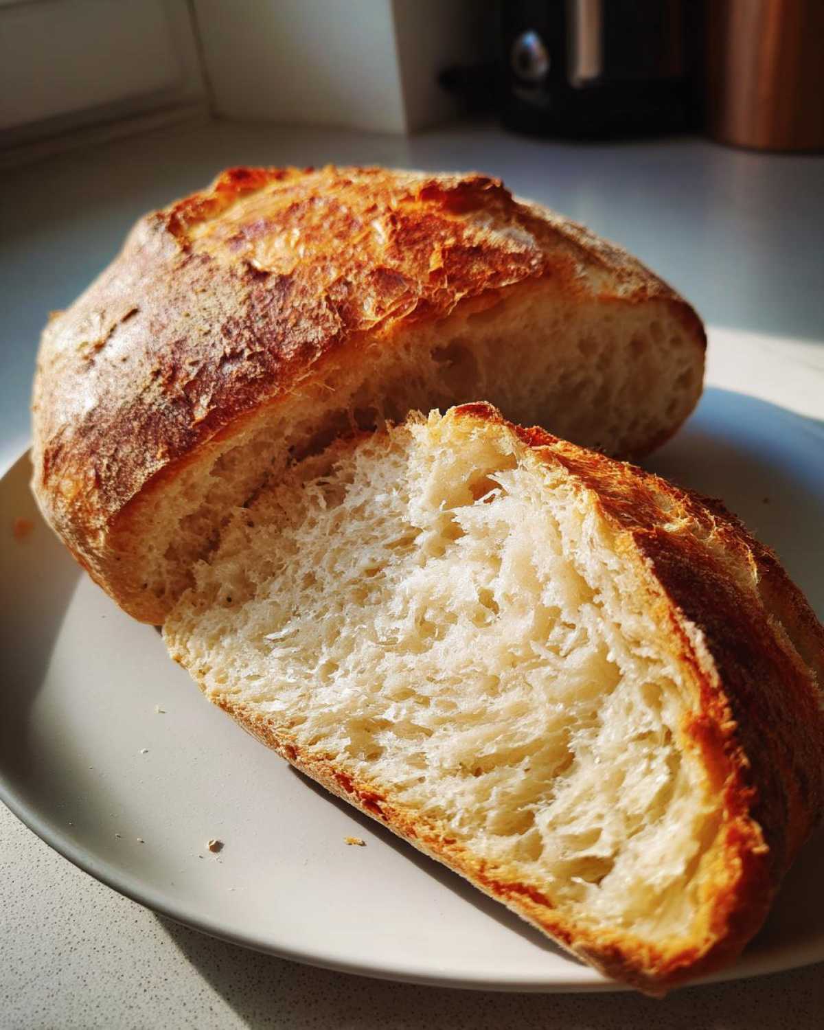 Przekrojony bochenek chleba domowego na drożdżach z chrupiącą skórką i puszystym miąższem na talerzu.