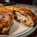 Przekrój Pizza Calzone nadziewanego szynką, pieczarkami i ciągnącym się serem na talerzu.