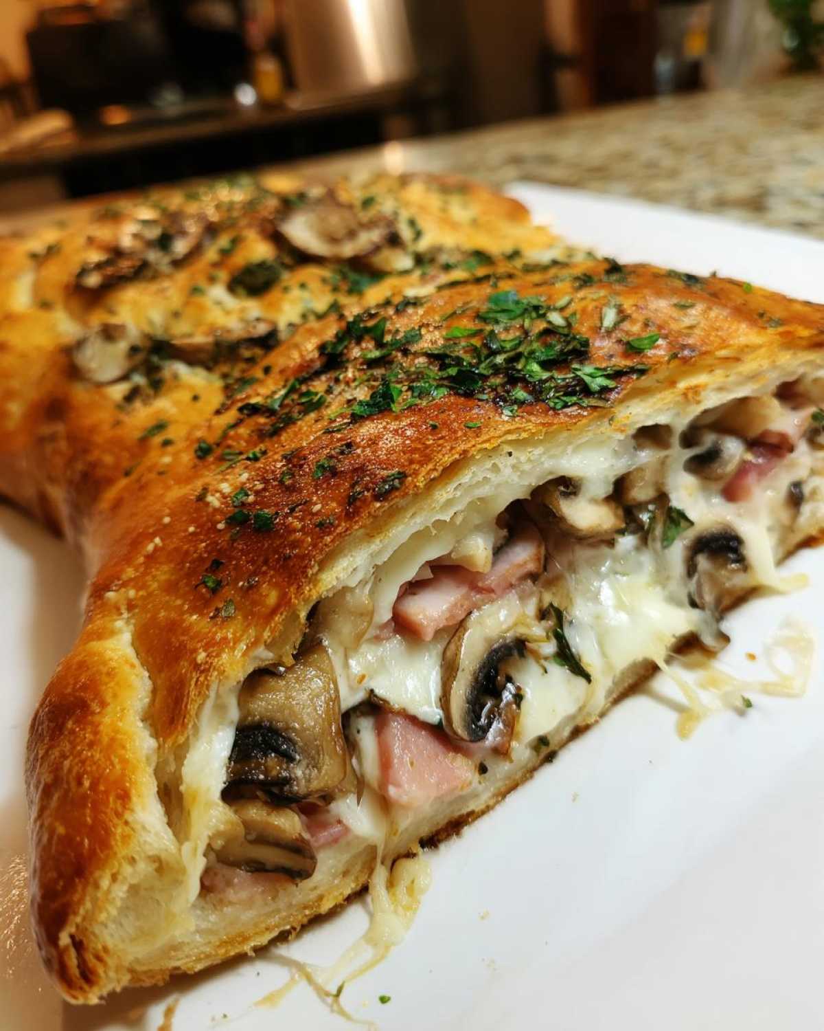 Zbliżenie na przekrojony Pizza Calzone wypełniony ciągnącym się serem, szynką i pieczarkami, posypany pietruszką.