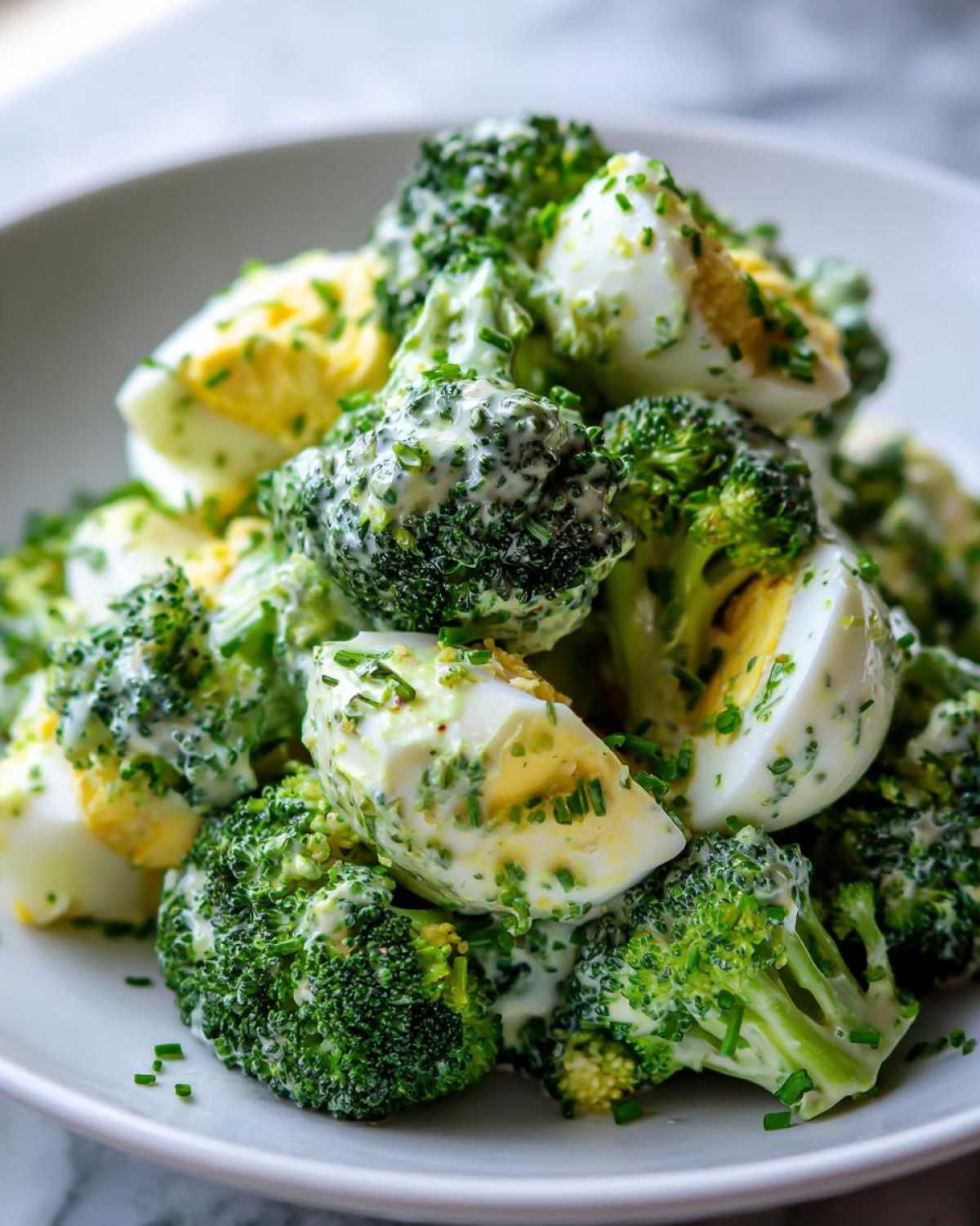 Zbliżenie na Sałatka z brokułem, jajkiem i sosem czosnkowym polana kremowym sosem i posypana szczypiorkiem.