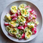 Zbliżenie na miskę pełną sałatki z jajkiem i rzodkiewką, polanej sosem i posypanej szczypiorkiem.