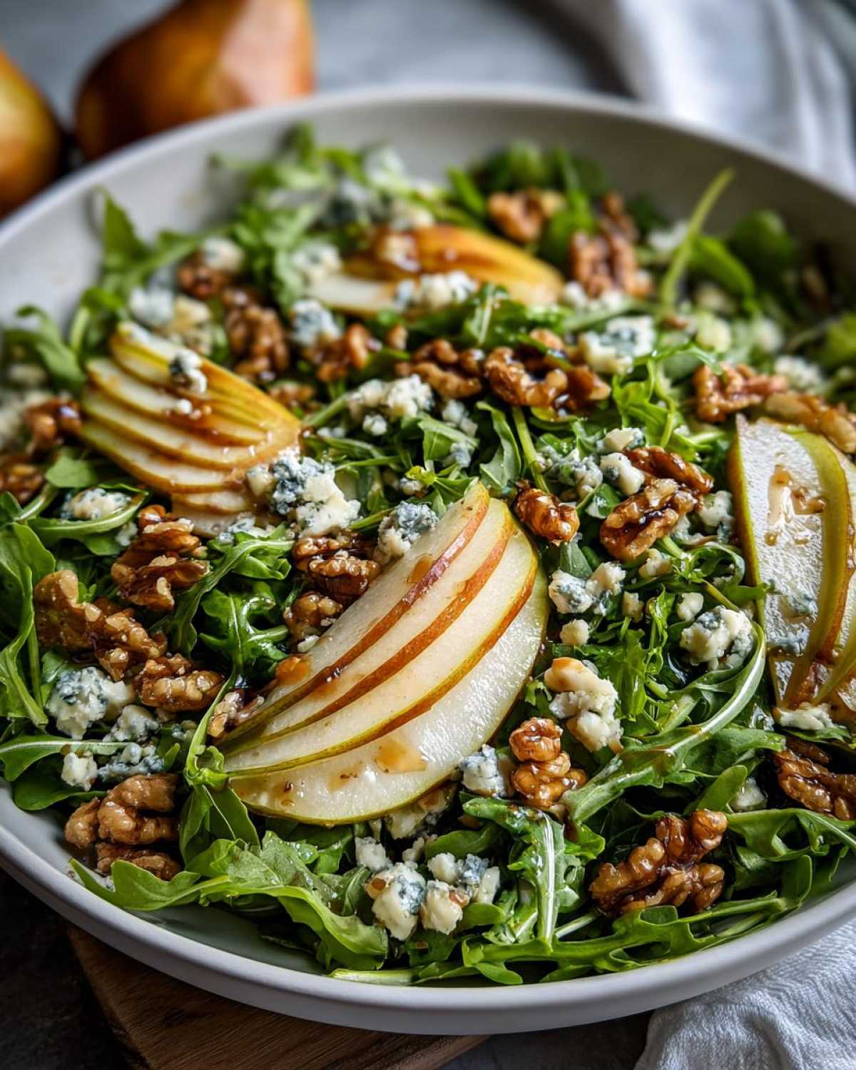 Miseczka pełna Sałatka z rukolą, gruszką i serem pleśniowym, udekorowana orzechami włoskimi i sosem.