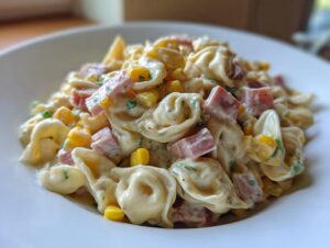 Zbliżenie na porcję Sałatka z tortellini i szynką z kukurydzą i kawałkami szynki w majonezowym sosie.