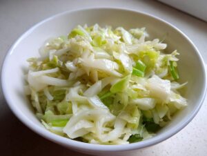 Zbliżenie na białą miseczkę wypełnioną świeżą surówką z pora i jabłka, z widocznymi kawałkami białego i zielonego pora.