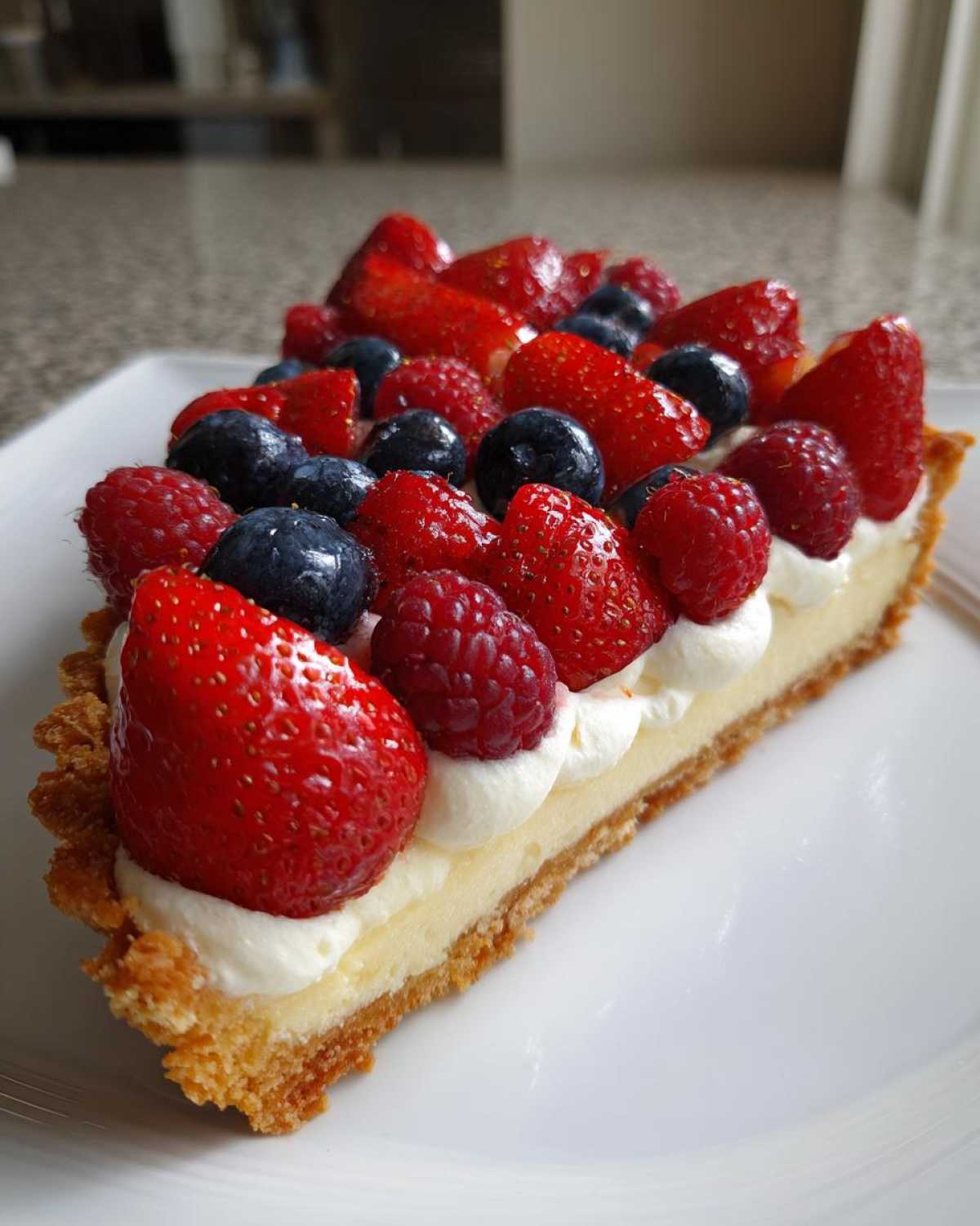 Kawałek pysznej Tarty z kremem mascarpone i owocami, udekorowany truskawkami, malinami i borówkami.