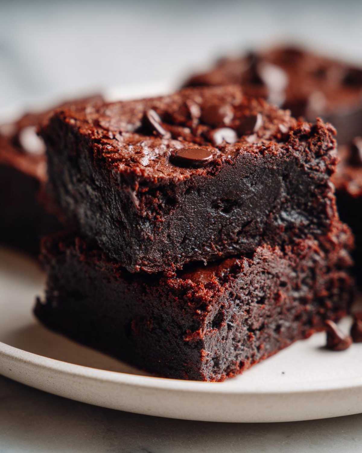 Zbliżenie na dwa ułożone na sobie, wilgotne kawałki Brownie z fasoli czerwonej posypane kawałkami czekolady.