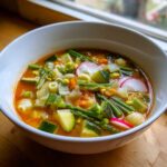Miseczka bogatej wiosennej zupy minestrone z dużą ilością świeżych warzyw i makaronem.