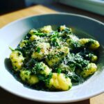 Zbliżenie na talerz pełen Gnocchi ze szpinakiem polane sosem i obficie posypane tartym serem.