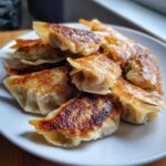 Zbliżenie na stos złocistych, podsmażonych Japońskie pierożki gyoza z wieprzowiną i kapustą na białym talerzu.