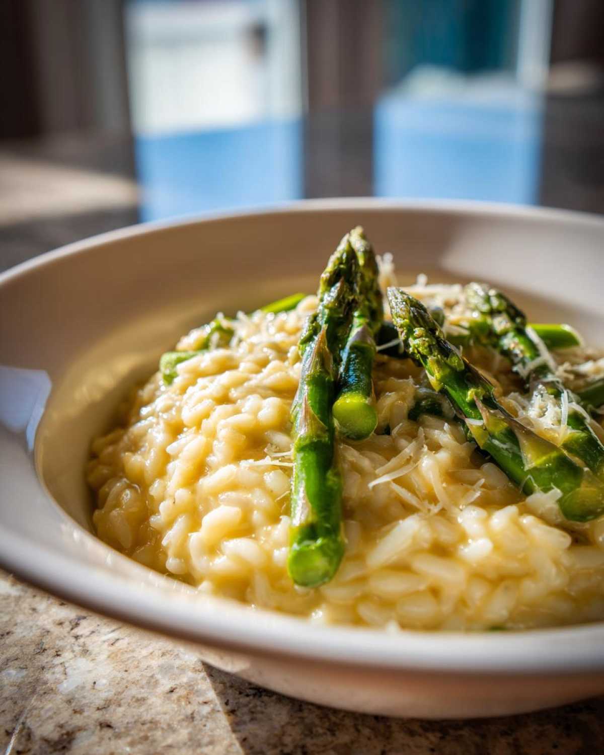 Kremowe risotto ze szparagami i dojrzewającym parmezanem podane w misce, z widocznymi zielonymi szparagami.