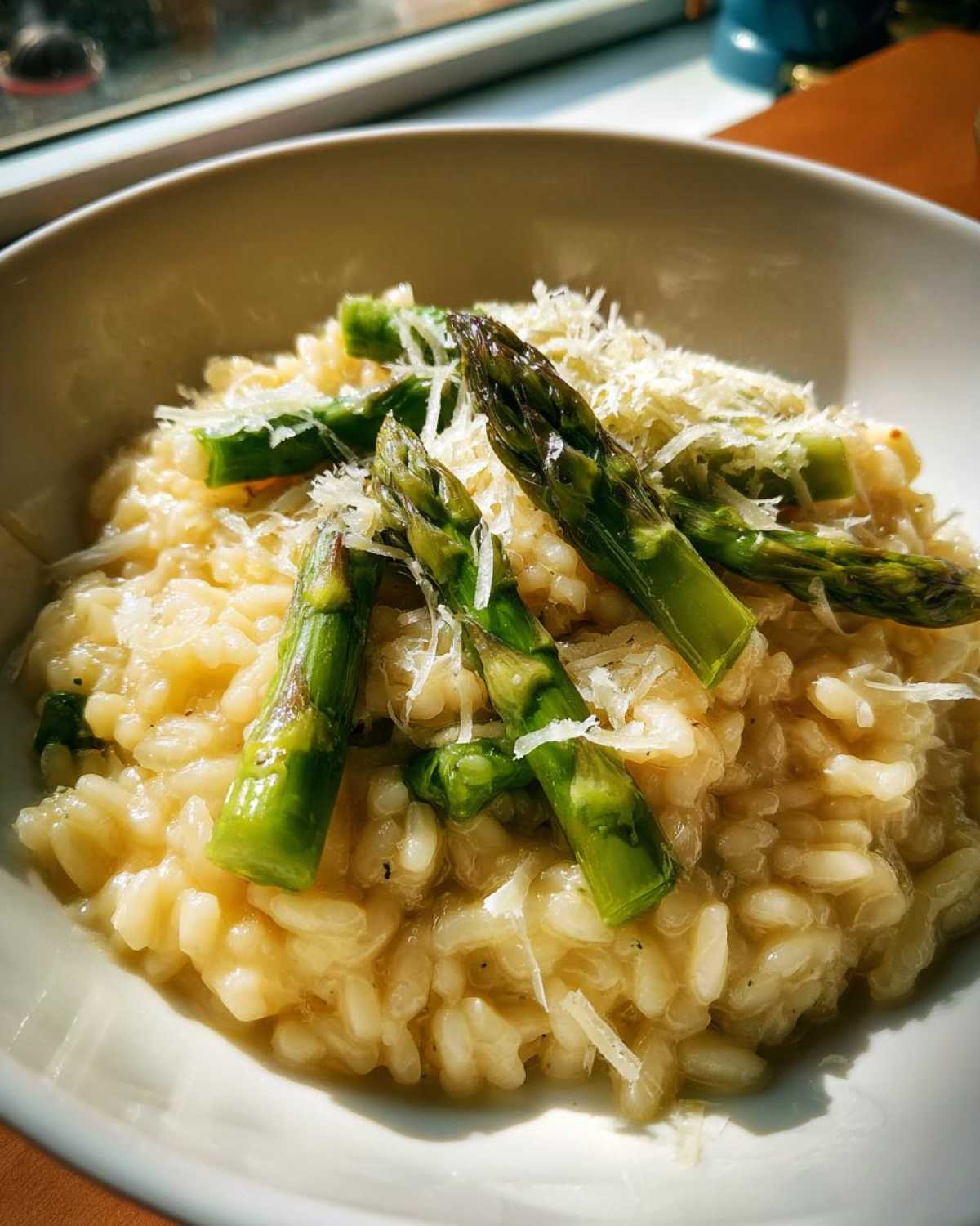 Zbliżenie na kremowe risotto ze szparagami i startym dojrzewającym parmezanem w białej misce.