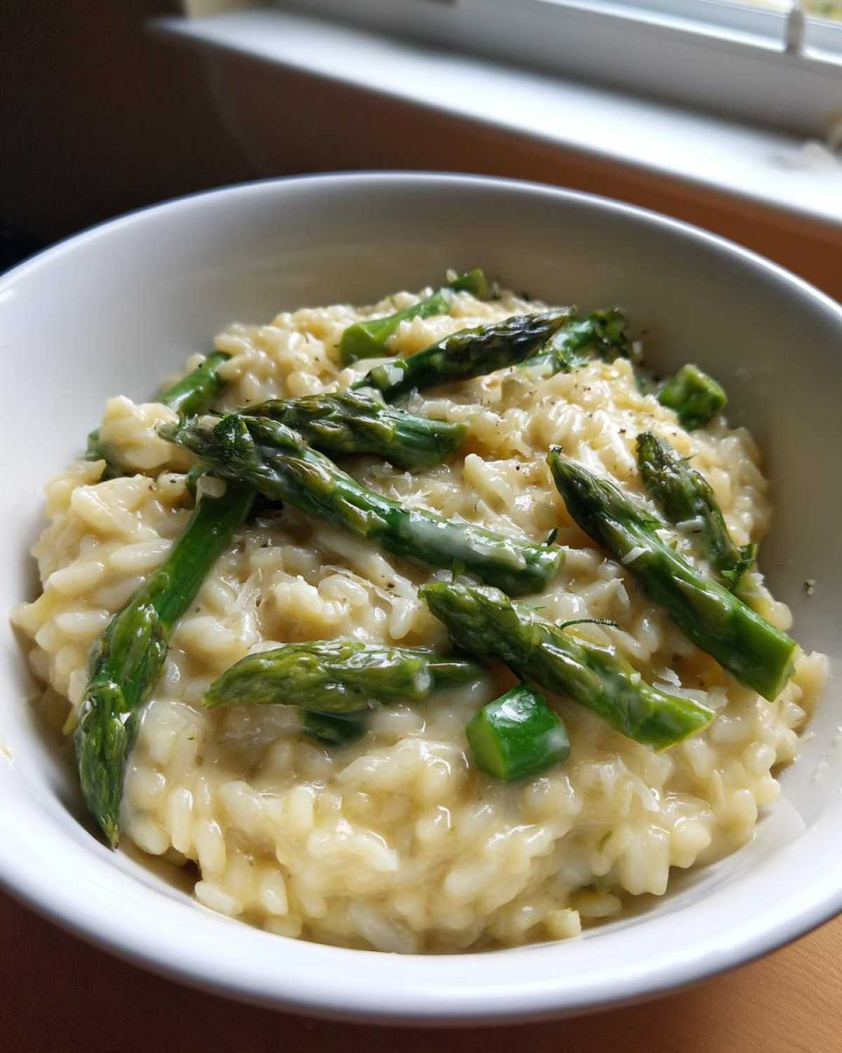 Zbliżenie na kremowe risotto ze szparagami i parmezanem podane w białej misce.