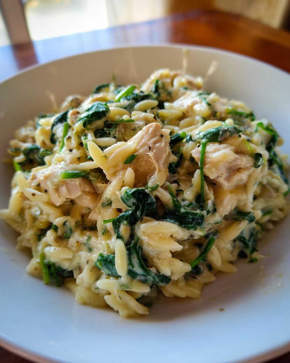 Zbliżenie na miskę kremowego makaronu orzo ze szpinakiem i kurczakiem, gotowego do podania.