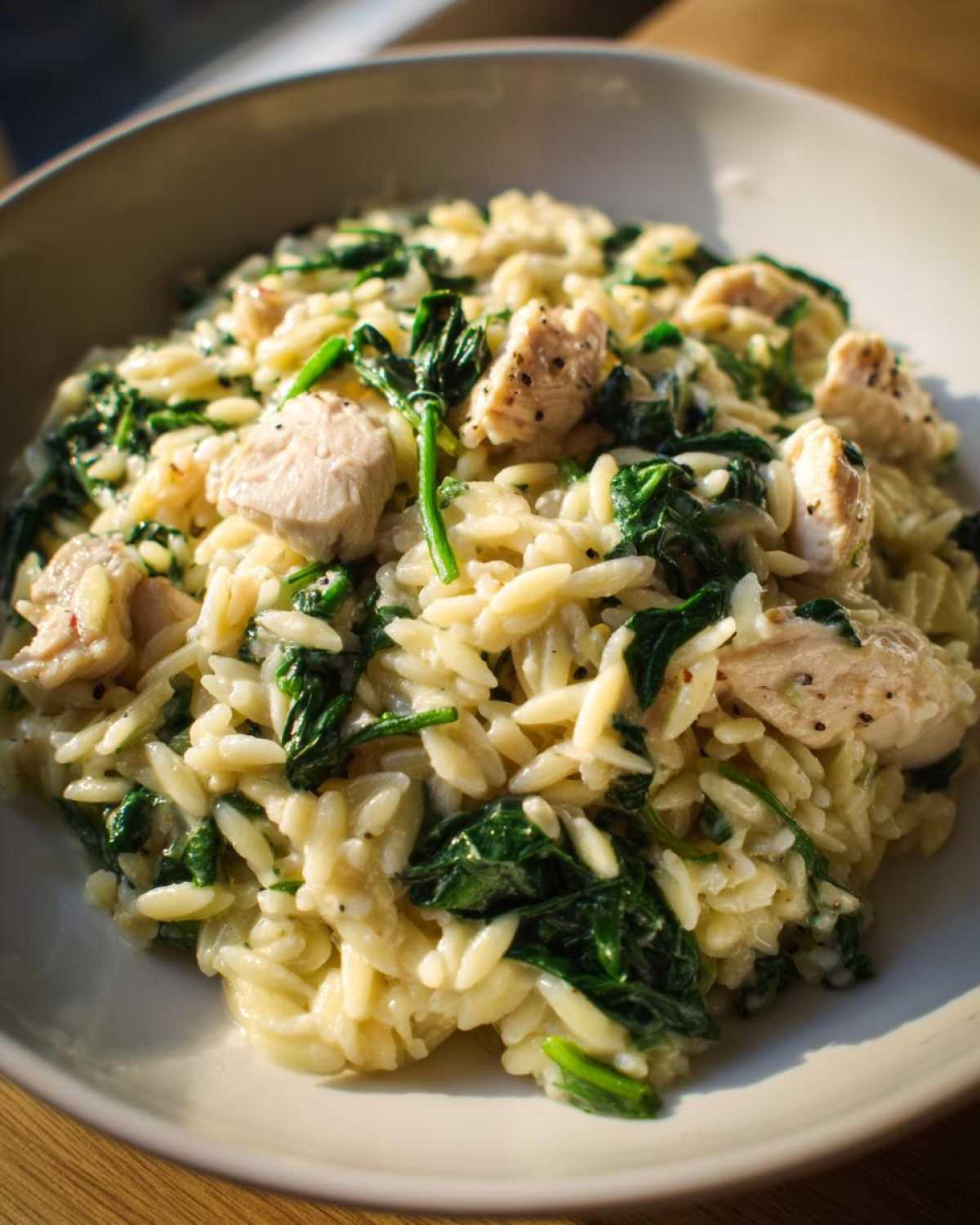 Zbliżenie na porcję kremowego makaronu orzo ze szpinakiem i kawałkami kurczaka w jasnej misce.