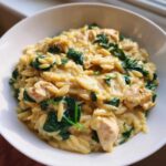 Zbliżenie na miskę kremowego makaronu orzo ze szpinakiem i kurczakiem, gotowego do podania.