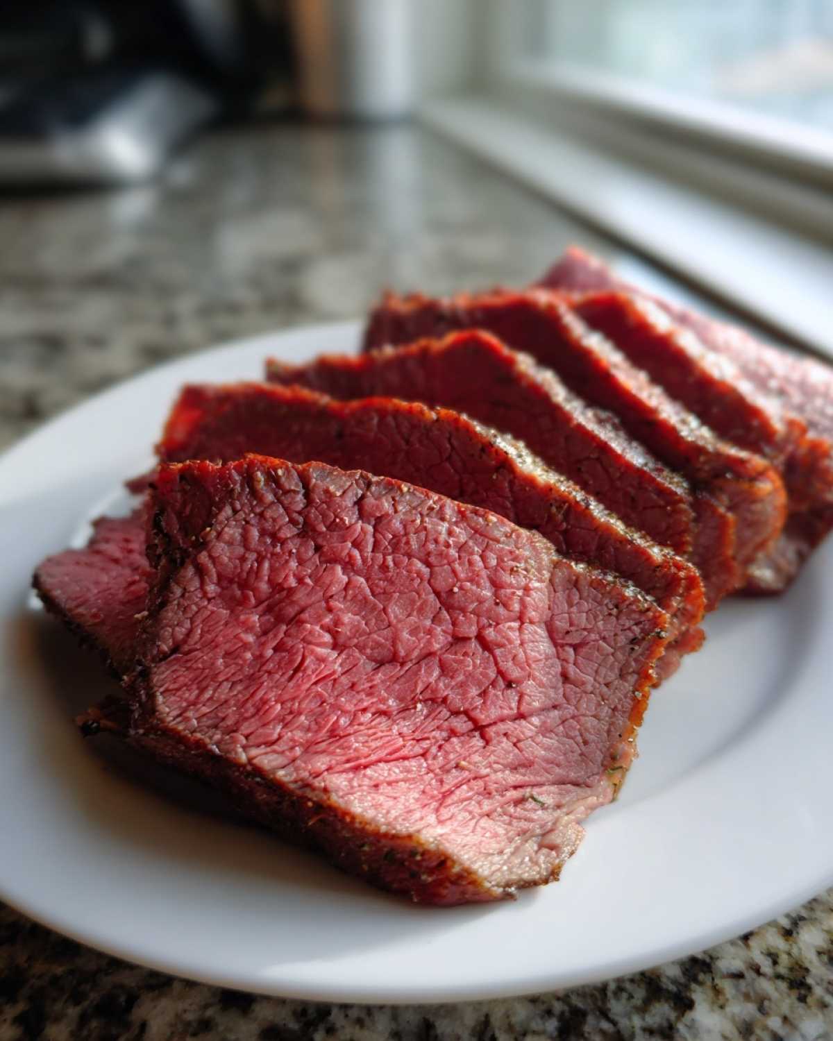 Zbliżenie na plasterki soczystej pieczeń wołowa wysmażonej na różowo, ułożone na białym talerzu.