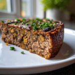 Zbliżenie na kawałek soczystego pasztet z pieczarkami, udekorowany natką pietruszki na białym talerzu.