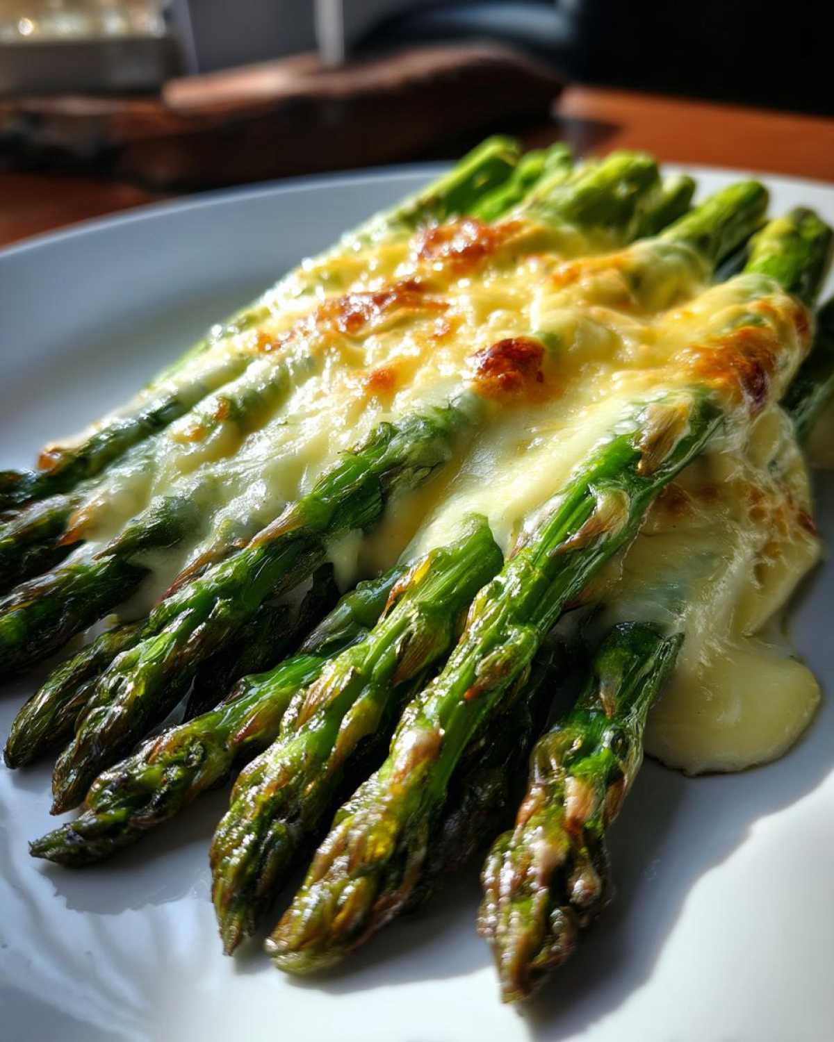Zbliżenie na zielone szparagi pieczone z roztopionym, zapieczonym serem camembert.