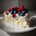 Kawałek Bezy Pavlova z owocami leśnymi, bitą śmietaną i chrupiącą bezą.