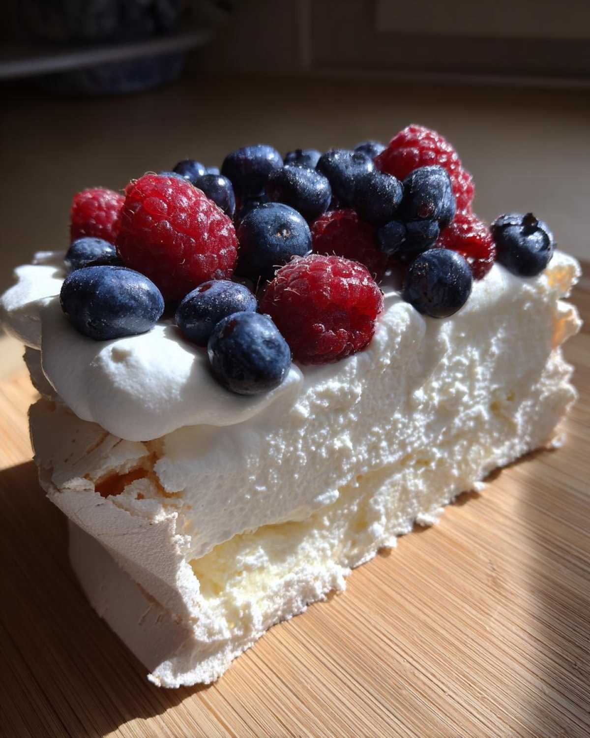 Kawałek Bezy Pavlova z owocami leśnymi, bitą śmietaną i chrupiącą bezą.