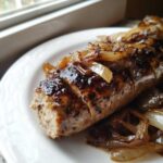 Zbliżenie na grillowaną białą kiełbasę z cebulką na białym talerzu.