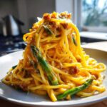 Talerz pełen kremowej Carbonara ze szparagami, obficie polany sosem jajecznym i posypany serem.