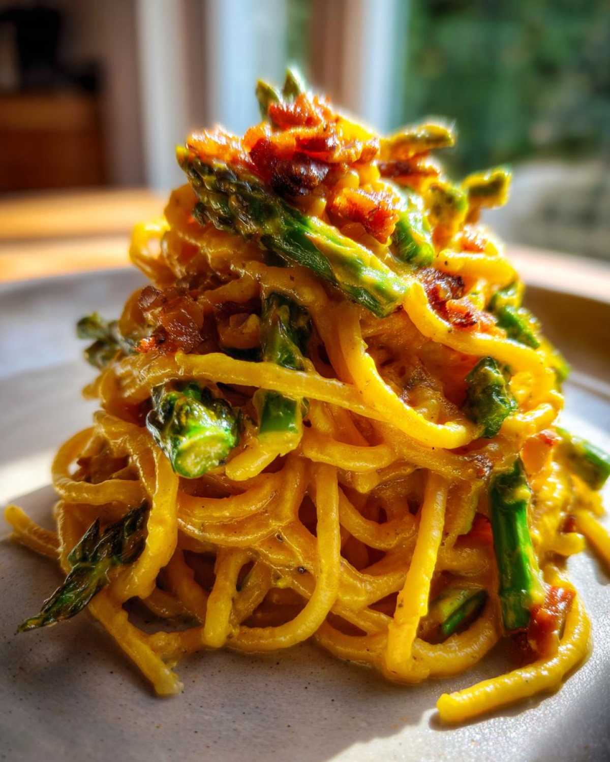 Porcja kremowej Carbonara ze szparagami i chrupiącym boczkiem, ułożona na szarym talerzu.