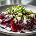 Zbliżenie na talerz z Carpaccio z buraka z kozim serem, polane sosem balsamicznym i rukolą.